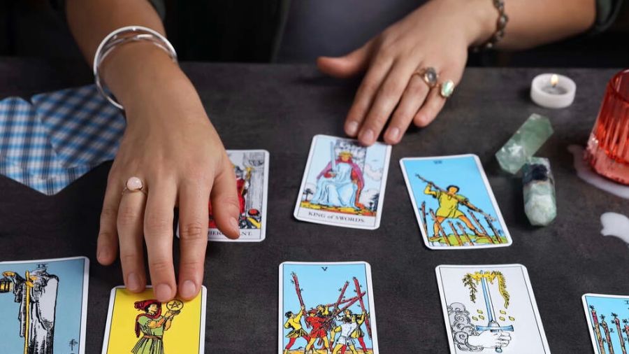 Tarot cards on a table with healing crystals, candle, and hands with rings and bangles, reading the cards.