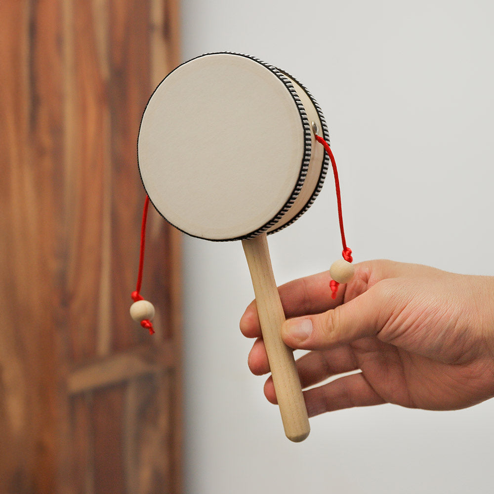 Handheld Adesu monkey drum shown in hand for scale, highlighting its compact size and wooden construction.