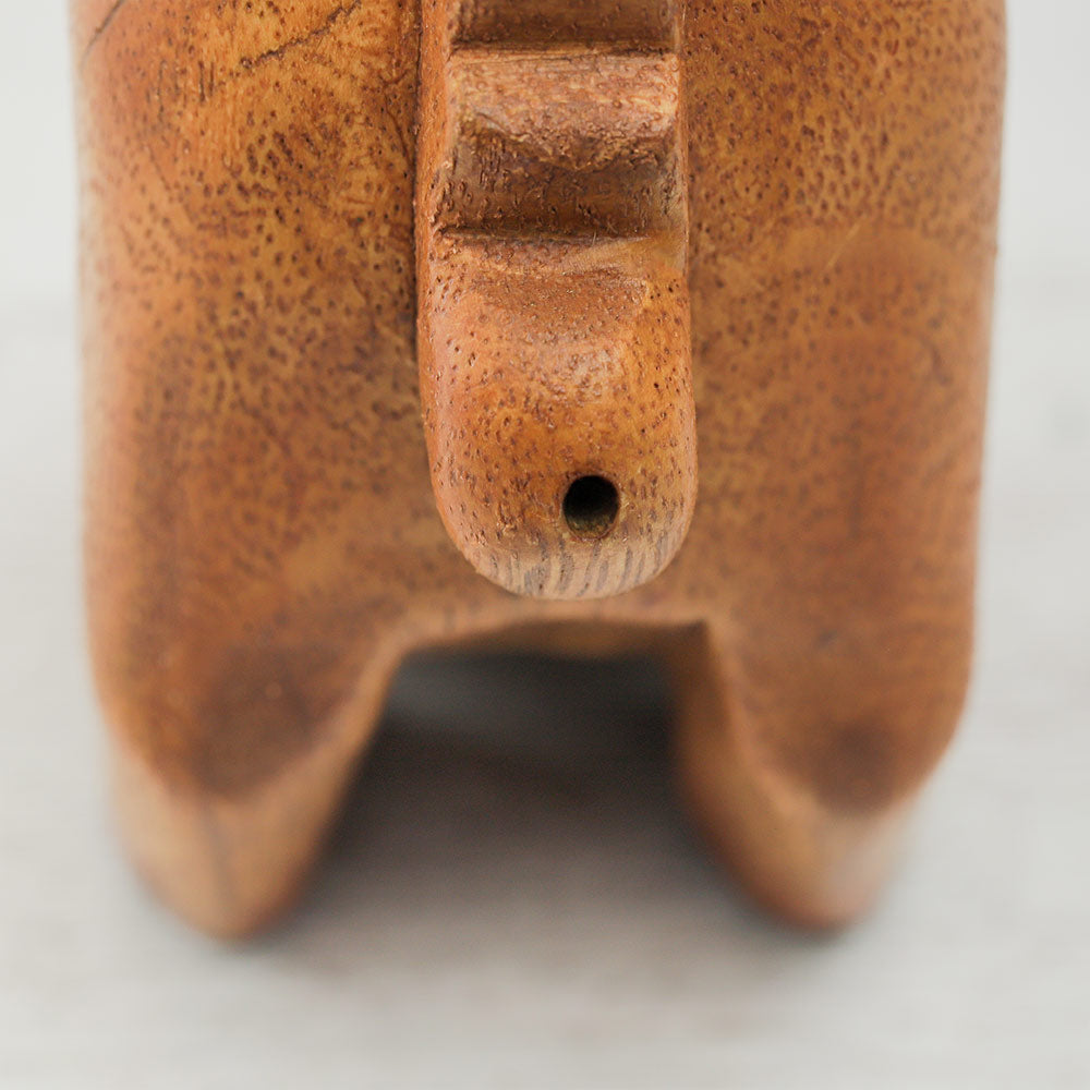 Close-up of the back of a purring cat guiro, showing the whistle hole. The wooden percussion instrument features carved details and a smooth finish.