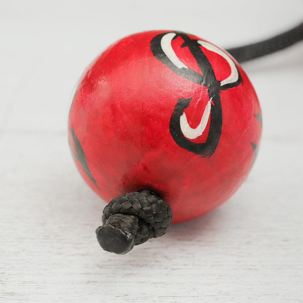 Close-up of an African Kashaka shaker ball with a red hand-painted design, highlighting its texture and details.