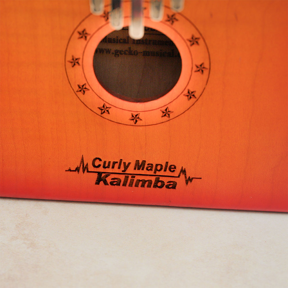 Close-up of the main sound hole on the Gecko Kalimba Sunburst Design with 'Curly Maple Kalimba' text visible.