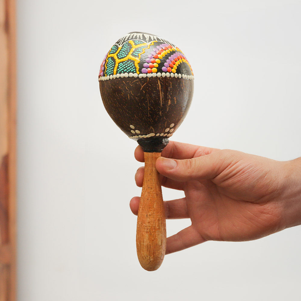 Colourful coconut shell maraca with a hand-painted sun design, mounted on a wooden handle. Produces rhythmic shaker sounds, ideal for musicians.
