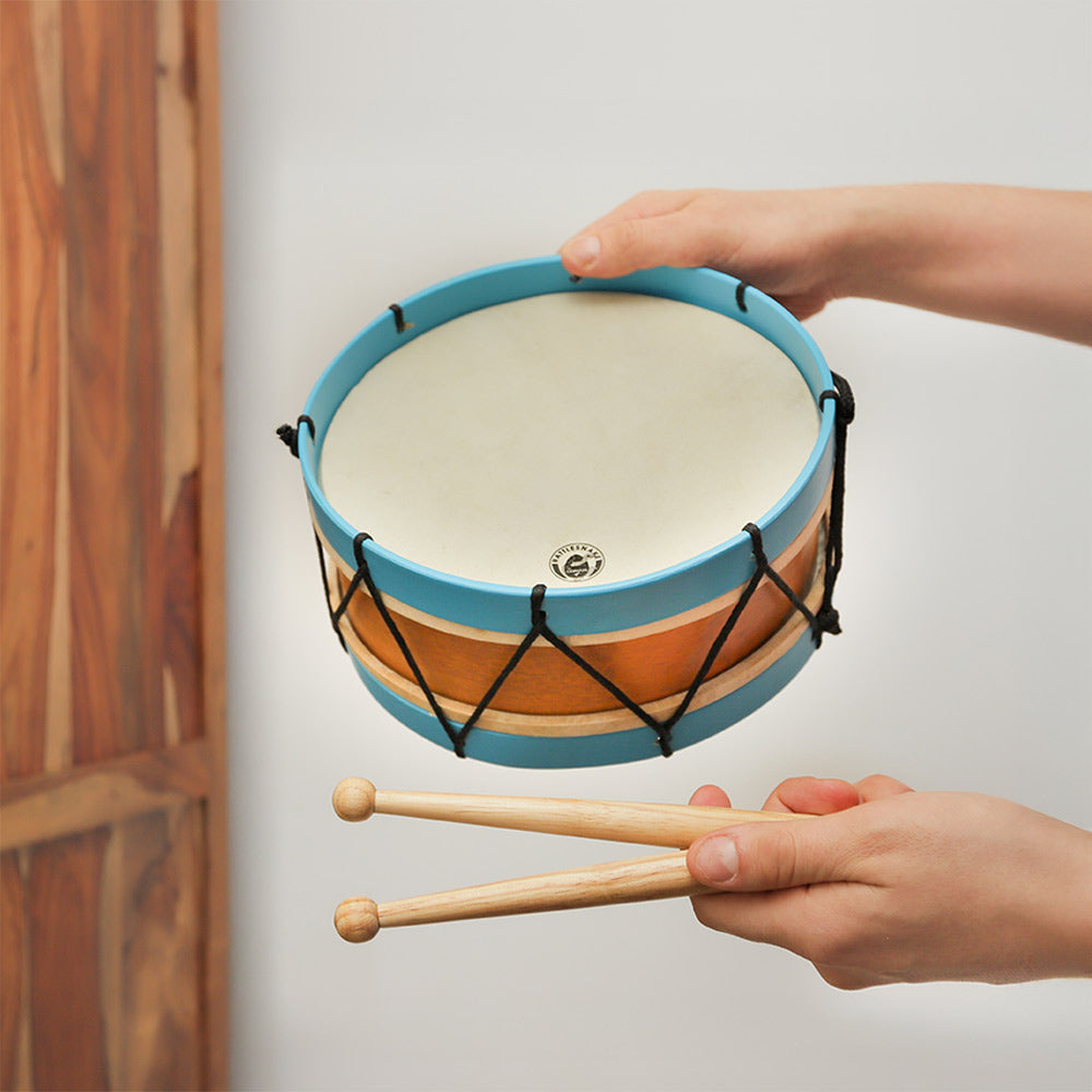 A close-up of the Rattlesnake Percussion Marching Drum in blue, held in hand to show scale. The drum includes two wooden beaters and features a sturdy design.