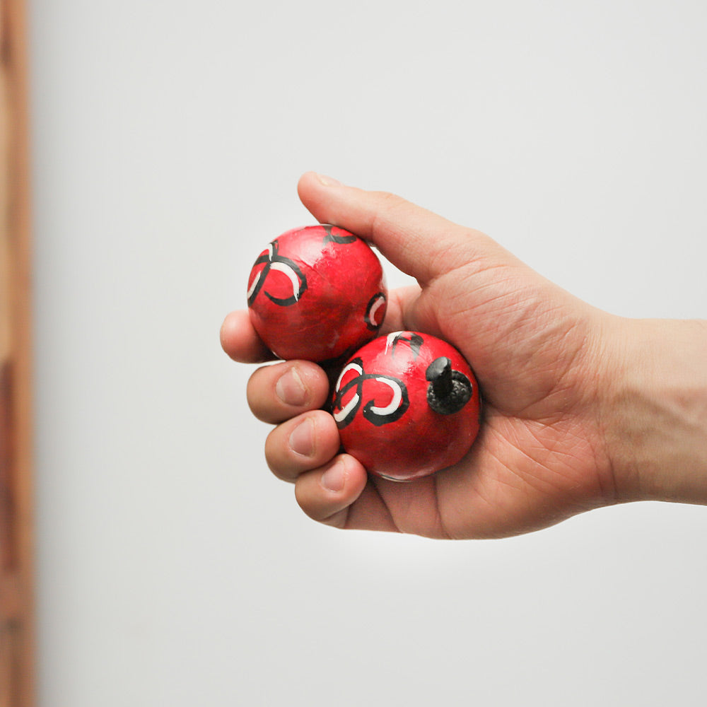 Close-up of a hand-painted red African Kashaka shaker, held in hand to show scale.