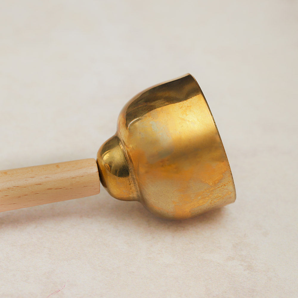 Close-up of the side view of a large Matsu brass bell, highlighting the smooth brass surface and the attached wooden handle.