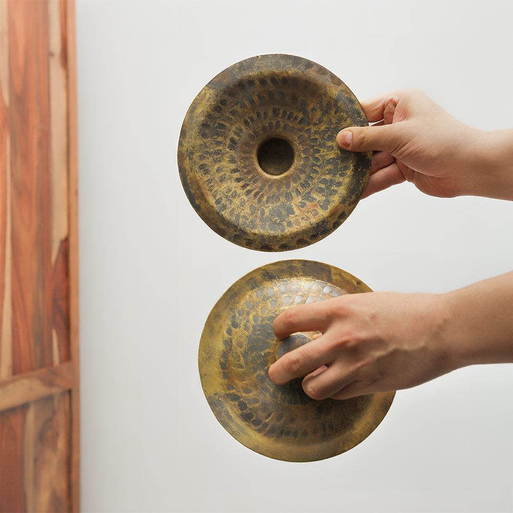 Vietnamese brass hand cymbals held in the hand, one showing the front and the other the back, to illustrate their size and scale.