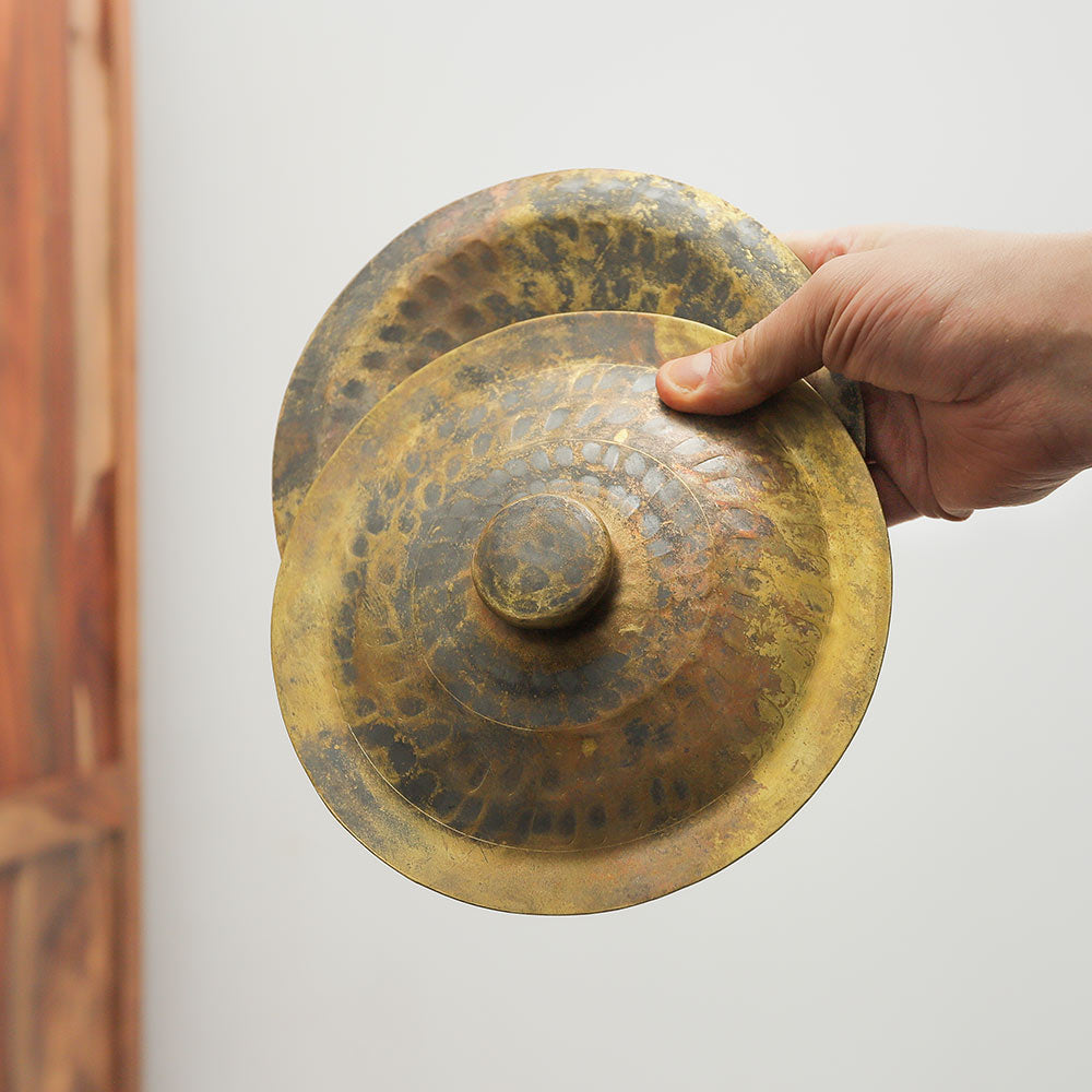 Vietnamese brass hand cymbals held in the hand to show their size and scale.