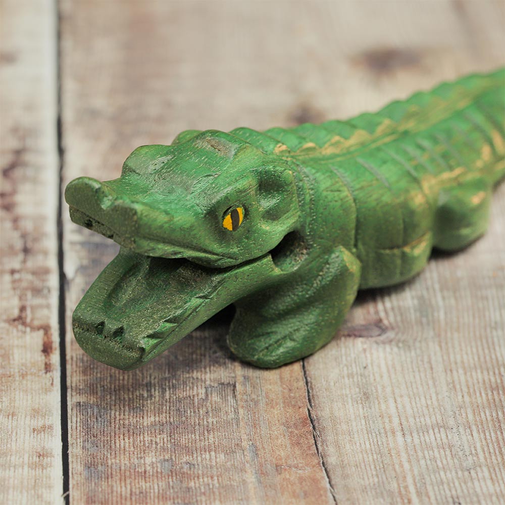 Close-up of a wooden crocodile guiro's face, featuring an open mouth, yellow eye, and textured ridged back.